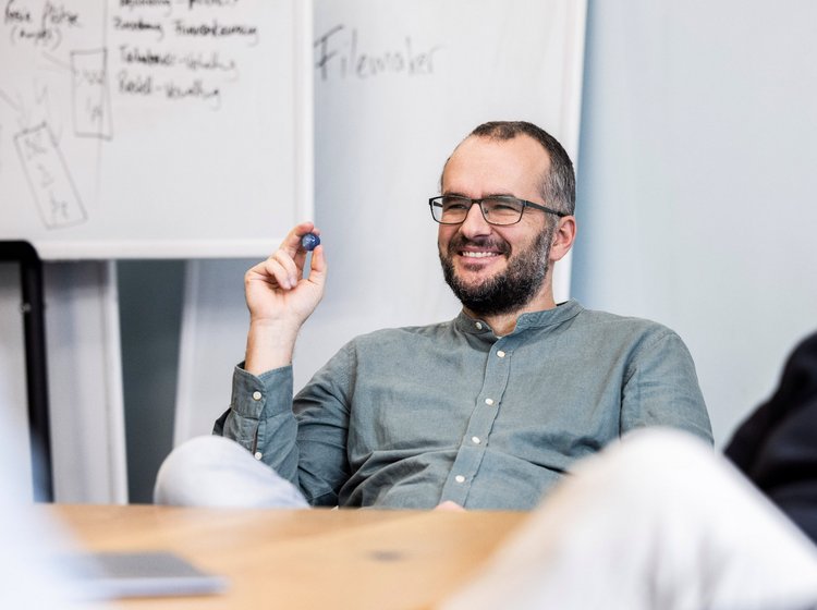 Präsentation mit Humor Teammitglied der Alpenblickdrei Werbeagentur zeigt lächelnd auf ein Flipchart bei einer lockeren Präsentation.