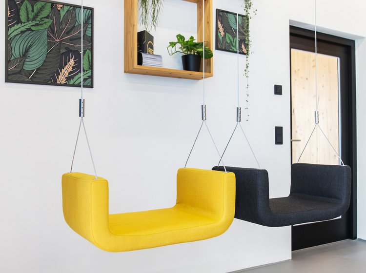 Designwand mit Schaukel und Pflanzen Kreativ gestaltete Wand mit gelber und schwarzer Schaukel, Pflanzen und Wandbildern in einem offenen Arbeitsbereich.