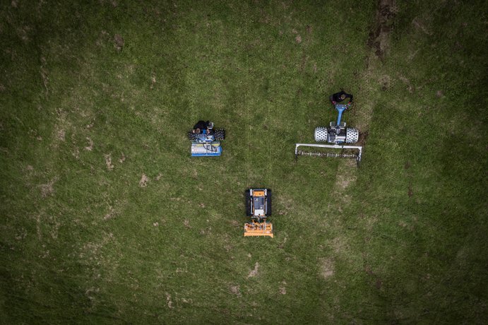 Drohnenaufnahmen von Geräte von Bentele Drei autonome Rasenmäher fahren auf einem grünen Feld und mähen das Gras.