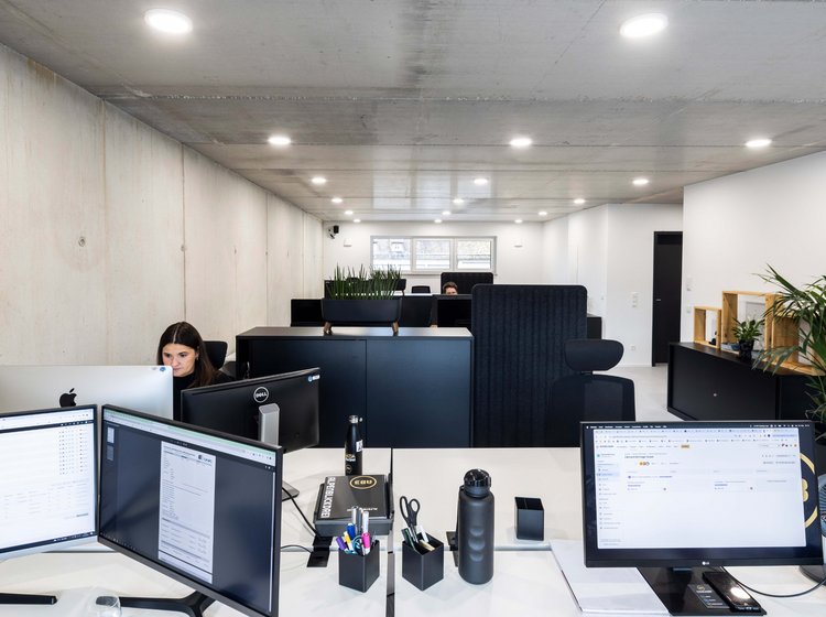 Modernes, helles Büro der Werbeagentur in Bad Waldsee mit mehreren Schreibtischen, Computerbildschirmen und einer Person, die konzentriert am Arbeitsplatz arbeitet.