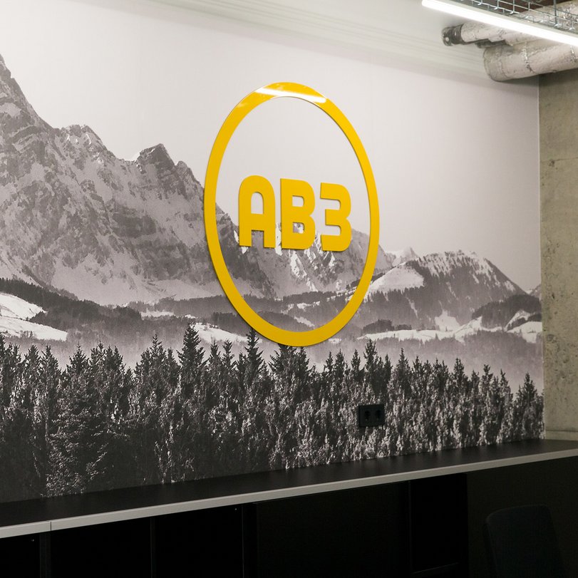Bergmotiv mit gelbem Firmenlogo Wandbild mit Berglandschaft in Schwarzweiß, darauf ein gelbes Firmenlogo – modernes Wanddesign im Büro.