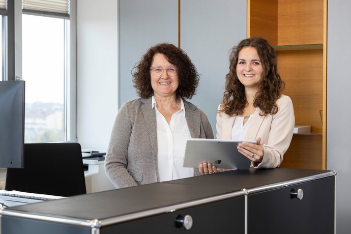 SWG-Mitarbeiterinnen am Arbeitsplatz Zwei Frauen sitzen an einem Schreibtisch und lächeln in die Kamera.