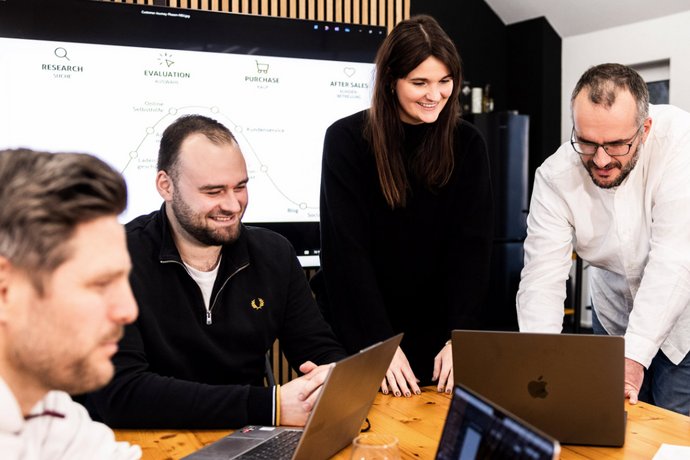 Kreatives Meeting Fünf Personen bei lebhafter Diskussion im Besprechungsraum der Alpenblickdrei Werbeagentur.