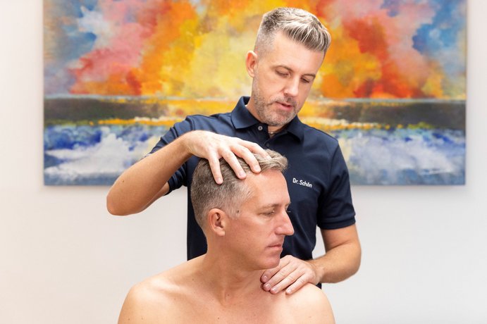 Manuelle Medizin Dr. Schön untersucht einen Mann an der Halswirbelsäule