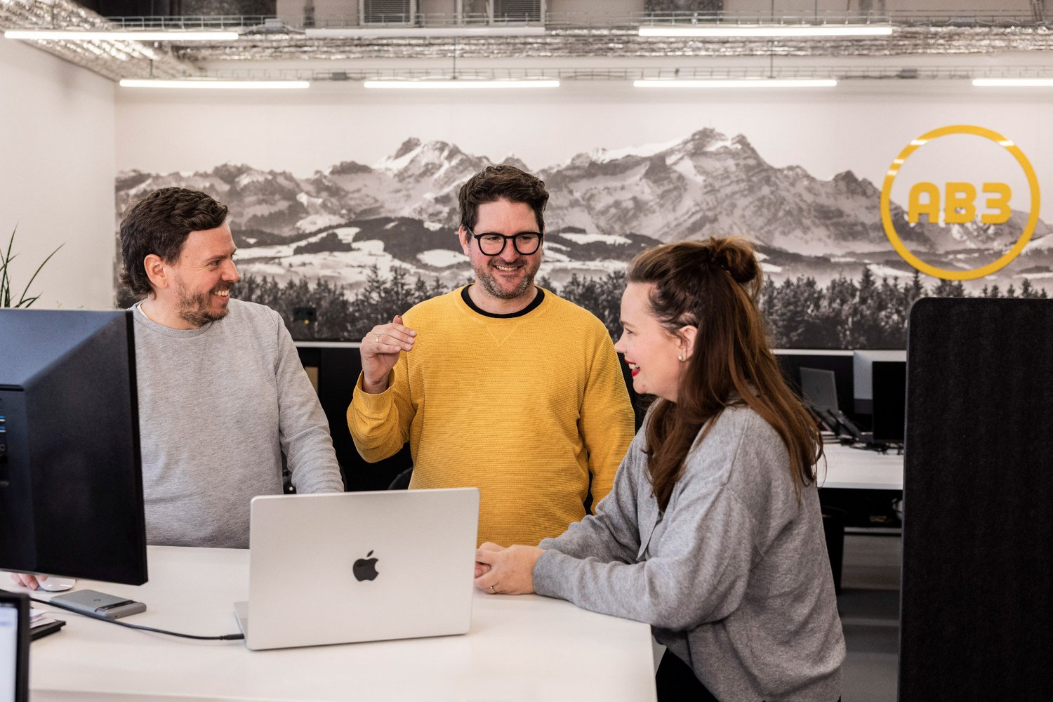 Pause und Gespräch Drei Personen unterhalten sich entspannt in der offenen Küche der Alpenblickdrei Werbeagentur.