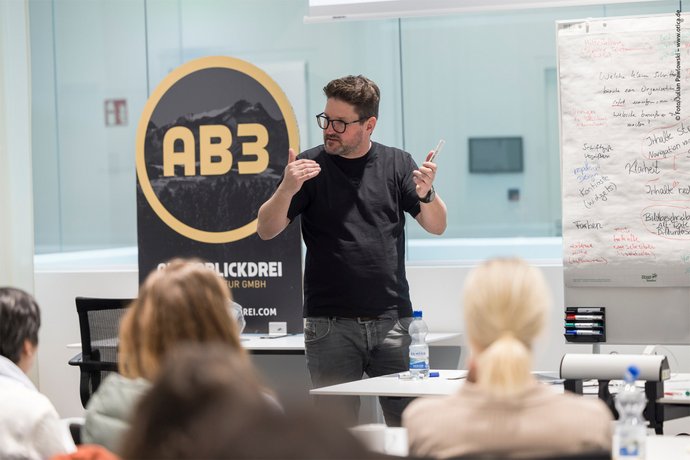 AB3 auf dem Barcamp Marvin Lang hält einen Vortrag, im Hintergrund sieht man ein Whiteboard und das AB3 Logo