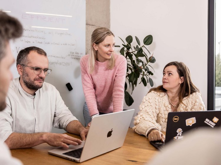 Drei Erwachsene sitzen an einem Tisch mit Laptops und führen eine Besprechung über eine Kampagne.