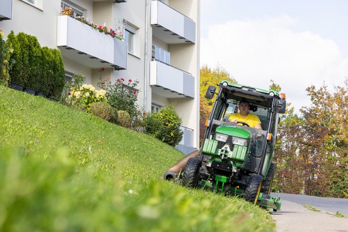 Grünpflege vor SWG-Wohnhaus Mann mäht Rasen vor einem modernen Mehrfamilienhaus der SWG.