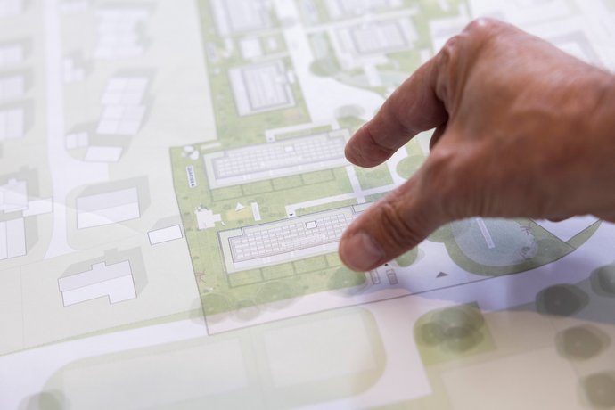 Planungsarbeit mit Bauzeichnung Hand zeigt auf einen Architekturplan auf einem Tisch.