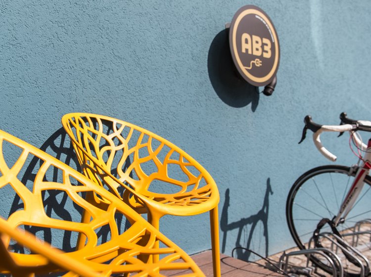 Urbaner Außenbereich mit Farbakzenten Außenbereich mit gelbem Stuhl, Wandlogo und Fahrrad vor einer blauen Wand, urbaner und verspielter Look.