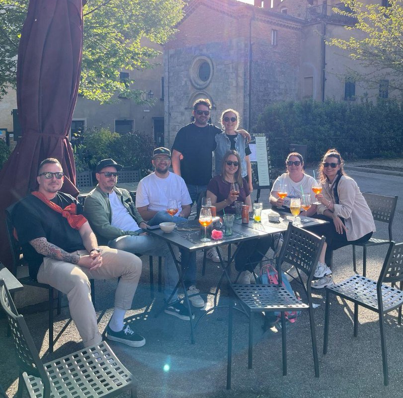 Gemütlicher Abend in der Toskana Gruppe von Menschen sitzt draußen an einem Gartentisch unter Bäumen bei schönem Wetter.